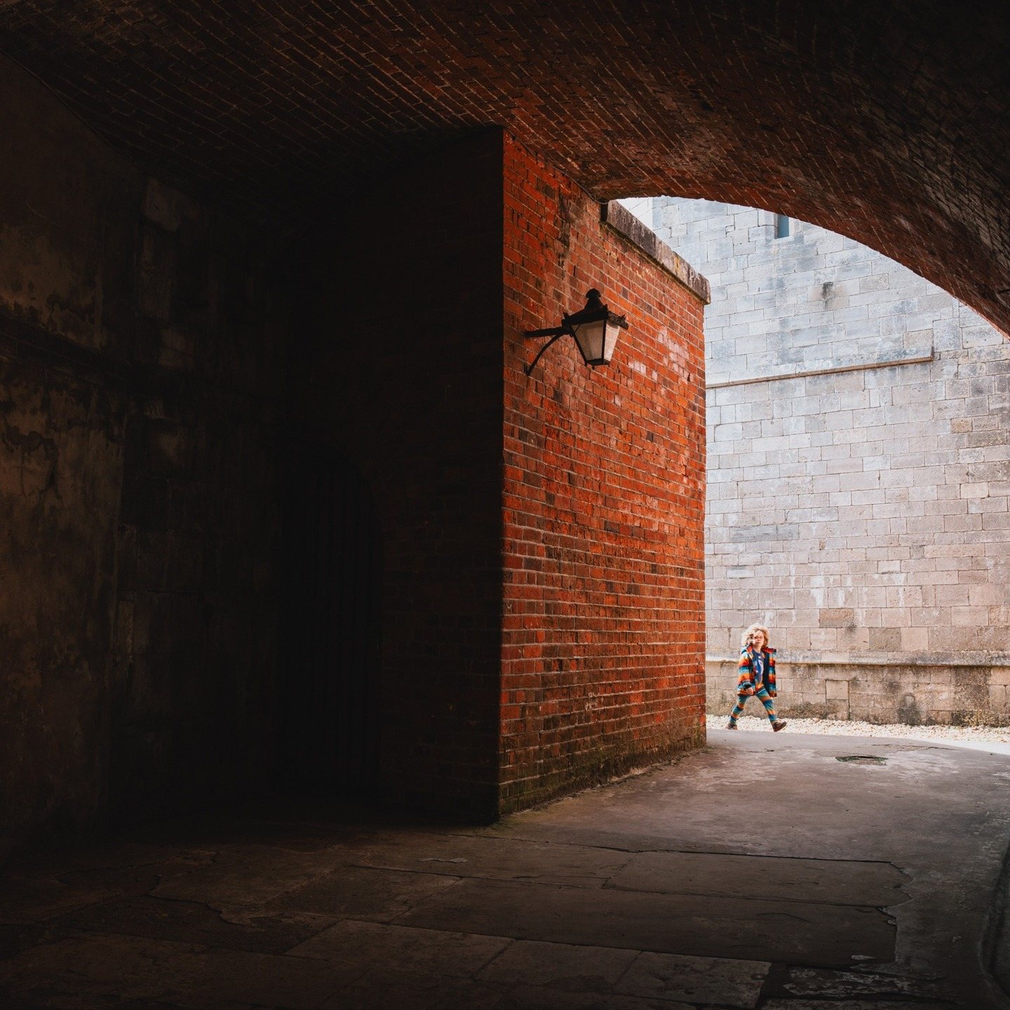 Child in a rainbow coat passing a brick archway